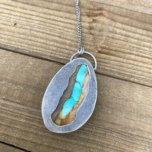 Necklace with a pendant featuring turquoise inlay on a wooden surface